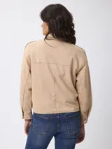 Campera de estilo camisero con efecto gamuzado, color beige, de corte recto y holgado. Presenta cuello clásico, cierre frontal con botones, mangas largas con puños abotonados y bolsillos frontales aplicados.