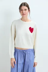 Sweater de punto gris con diseño de corazón blanco en el pecho, cuello redondo y mangas largas.
