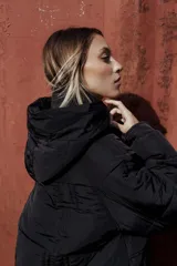 Campera larga acolchonada color marrón, con diseño midi, capucha amplia, cierre frontal con cremallera y broches, y bolsillos delanteros con tapa.