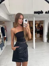 Pollera corta de cuero sintético con diseño de paneles y bolsillos frontales grandes. Presenta un corte recto y tiro medio.