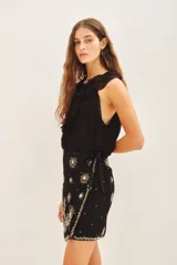 Falda corta cruzada con diseño envolvente y lazo lateral para ajuste. Presenta bordados florales detallados en toda la superficie, tanto en el frente como en la espalda. Está completamente forrada para mayor comodidad.