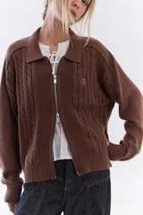 Cardigan de tejido de punto color marrón, con cuello solapa, cierre frontal de cremallera y diseño de trenzas. Cuenta con puños y dobladillo en rib elástico y un pequeño bordado en el pecho.