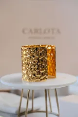 Brazalete ancho de diseño abierto con textura martillada y acabado brillante en tono dorado.