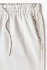 Pantalón deportivo en felpa pesada de mezcla de algodón, color gris claro, de corte holgado con cintura elástica ajustable mediante cordón y bolsillos laterales.