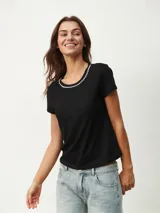 Remera negra de corte clásico con cuello redondo ribeteado con pequeñas perlas blancas.