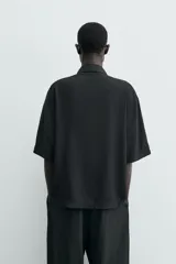 Camisa de corte relajado confeccionada en tejido fluido con mezcla de viscosa, color negro. Presenta cuello solapa, manga corta, cierre frontal con botones y un bordado a contraste en el pecho.