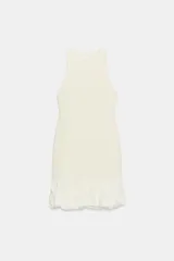 Vestido corto de color blanco con cuello redondo y diseño sin mangas. Presenta un cuerpo de tejido bouclé texturizado y un bajo acabado con volantes de tejido ligero.