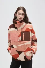 Buzo de polar tipo canguro con cuello alto y cierre frontal parcial. Presenta un diseño estampado con bloques de colores en tonos rosado, naranja, marrón y crema, y cuenta con un bolsillo frontal con cierre en contraste de color marrón.