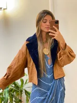 Campera oversize de cuero tostado con solapas y forro interno de corderito sintético azul marino, mangas anchas y detalles de costuras trenzadas.