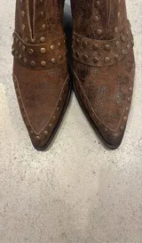 Botas cortas de cuero color chocolate con acabado desgastado y detalle de tachas metálicas. Presentan un taco cuadrado de madera y punta fina.