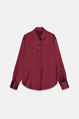 Camisa de cuello solapa y manga larga, confeccionada en tejido satinado con acabado brillante. Presenta cierre frontal con botones y bajo asimétrico.