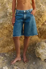 Bermuda de denim azul con corte a la rodilla, diseño de tiro medio y ruedo deshilachado al corte.