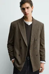 Blazer de corte relajado confeccionada en tejido con lana, con diseño de cuadros pequeños. Presenta cuello con solapas de pico, cierre frontal de botonadura cruzada, manga larga con botones en los puños y bolsillos de vivo en el pecho y la cadera.