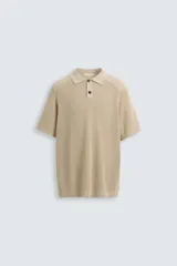 Polo de manga corta, color beige claro, con cuello solapa y cierre frontal de dos botones. Tejido de punto con textura acanalada vertical.