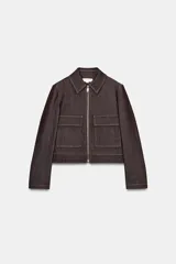 Chaqueta corta de denim oscuro con cuello solapa, cierre frontal con cremallera y bolsillos delanteros de plastrón con solapa. Presenta mangas largas con hombreras y costuras a la vista.