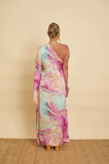 Vestido largo con diseño marmolado en tonos celestes, rosados y amarillos, de corte asimétrico con un solo hombro y manga larga acampanada.