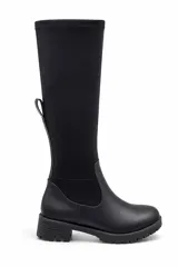 Bota alta de caña elástica color negro, con base de cuero sintético, suela track y taco bajo.