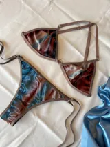Conjunto de bikini confeccionado en terciopelo con efecto degradado en tonos azul, marrón y rosado. El corpiño es de estilo triangular con aros metálicos decorativos en el centro y breteles regulables. La bombacha es de corte clásico con laterales ajustables mediante tiras.