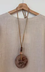 Collar largo con cinta de gamuza regulable y dije circular de acrílico con diseño marmolado en tonos tierra.