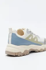 Zapatilla deportiva de inspiración outdoor con diseño de paneles en tonos neutros, que combina malla y materiales sintéticos. Presenta una suela robusta con relieve dentado para mayor tracción y estabilidad.