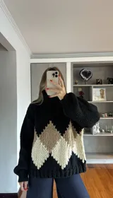 Buzo de tejido de punto grueso con cuello alto, diseño de rombos en tonos negro, beige y crema, y mangas largas con puños ajustados.