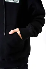 Hoodie negro de frisa con capucha y bolsillo canguro. Presenta un aplique rectangular en el pecho con texto en verde lima.