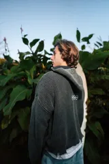 Campera de punto gris oscuro con capucha, cierre frontal completo y bolsillos delanteros tipo canguro. Presenta diseño texturizado en canalé grueso, detalles desgastados en los bordes y el texto "ssy waves" bordado en el pecho.