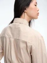Camisa de corte clásico con estampado de rayas verticales en tonos beige y blanco. Presenta cuello camisero, cierre frontal con botones y corbata integrada del mismo tejido y estampado.