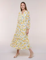 Vestido maxi de gasa con estampado floral en tonos amarillos y verdes sobre base blanca, escote en V cruzado, mangas largas y cintura elastizada con lazo.