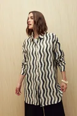 Vestido camisero de corte relajado con estampado de ondas verticales en tonos neutros. Presenta cuello clásico, cierre frontal con botones y mangas largas. Confeccionado en tejido fluido con caída liviana.