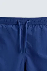 Short de baño azul con cintura elástica ajustable con cordón, bolsillos laterales y ribetes en contraste en los bordes.