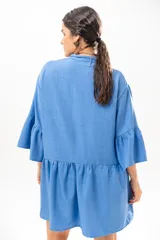 Vestido corto azul, estilo camisero, con cuello camisero, cierre frontal con botones y mangas acampanadas con volados. Presenta un diseño holgado con cortes fruncidos en el cuerpo.