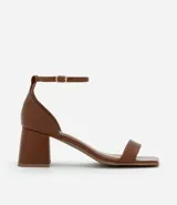 Sandalia de cuero marrón con puntera cuadrada, tira fina sobre los dedos y tobillo con hebilla, y tacón geométrico.