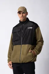 Campera de polar con recortes en tela técnica tipo sire en la parte superior frontal. Presenta cierre frontal completo, cuello alto y bolsillos funcionales en el pecho. Diseño bicolor en tonos verde oliva y negro con logo de la marca en el pecho.