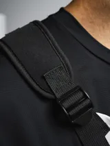 Bolso de pecho táctico color gris claro con detalles en negro, con correas ajustables y hombreras de neopreno. Cuenta con tres compartimentos: uno trasero de red y dos frontales con cierre.