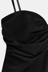 Body negro con escote corazón, detalle de frunces en el busto y tirantes finos ajustables. Presenta un diseño ajustado con cierre inferior mediante botones a presión.