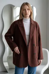 Tapado de paño color marrón, de corte oversize, con solapas clásicas, cierre frontal de doble botonadura y bolsillos laterales de parche.