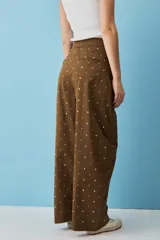 Pantalón marrón de corte ancho, tiro alto y diseño holgado, adornado con pequeños apliques metálicos distribuidos por toda la prenda.