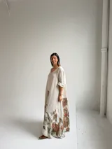 Vestido largo beige con diseño holgado, escote en V y mangas largas, adornado con un gran estampado floral en tonos marrones y verdes en la parte inferior.
