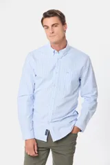 Camisa de corte clásico confeccionada en tela oxford de algodón, con diseño de rayas verticales finas en color celeste y blanco. Presenta cuello abotonado, cierre frontal con botones y bolsillo en el pecho.