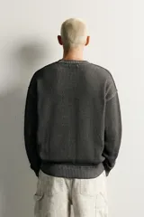 Sweater relaxed fit de algodón color gris con efecto lavado, cuello redondo, manga larga y diseño de textos estampados a contraste en el frente.