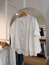 Camisa de algodón color blanco crudo, de manga corta, con diseño amplio oversize, cuello redondo con volados y cierre frontal con botones.