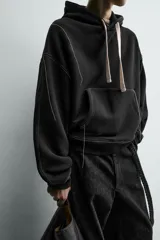 Sudadera tipo hoodie de corte relajado, color negro, con interior perchado. Presenta capucha ajustable con cordones en color crudo, bolsillo frontal tipo canguro y costuras a contraste en color blanco. Posee puños y ruedo en rib.