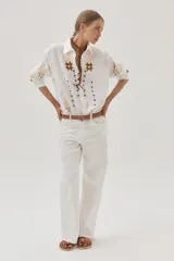 Camisa blanca de lino con bordados florales en tonos dorados y marrones en el frente y las mangas.