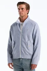 Campera estilo Harrington de corte clásico con diseño de rayas finas verticales en tono celeste y blanco. Cuenta con cuello alto, cierre frontal completo, bolsillos diagonales con solapa y botones, además de puños y dobladillo elastizados. Presenta el logo bordado del pingüino característico en el pecho.