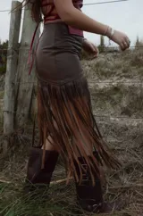 Pollera midi de cuero marrón con diseño asimétrico y flecos largos que aportan movimiento y textura.