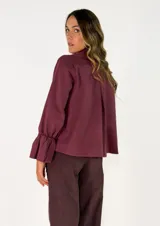 Chaqueta color tostado de corte recto y diseño cruzado con doble botonadura frontal. Presenta cuello solapa y mangas largas con puños acampanados y fruncidos.