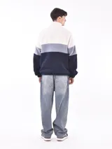 Buzo de tejido polar texturizado, color azul petróleo, con cuello alto y cierre parcial frontal. Presenta un diseño de bloques de color horizontal: blanco crema en la parte superior, gris claro en el medio y azul petróleo en la parte inferior y mangas.