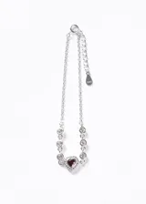 Pulsera de plata 925 con cadena de eslabones finos, decorada con pequeñas zirconias blancas engastadas en bisel y un dije central en forma de corazón con una zirconia roja rodeada de zirconias blancas. Incluye una cadena de extensión con una pequeña placa grabada.