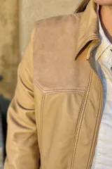 Camisa de cuero ovino color beige claro, estilo western, con canesú en los hombros en gamuza de tono similar. Presenta costuras contrastantes y cierre frontal con broches. Posee bolsillos laterales.